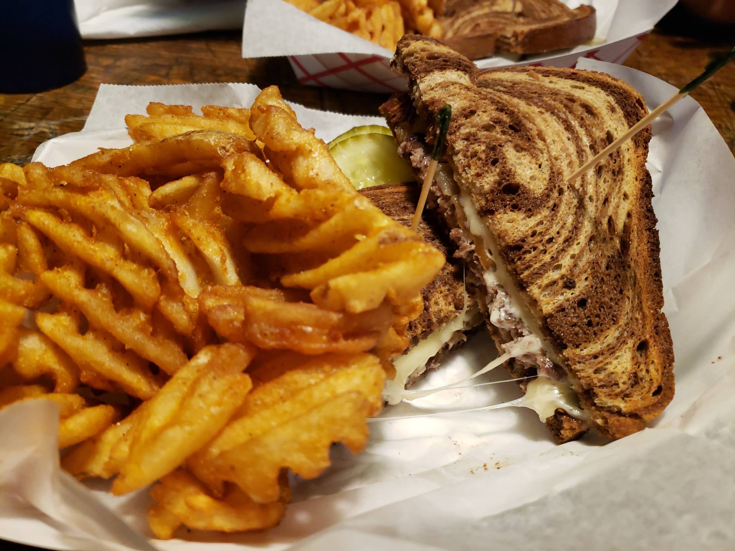  Paddyâ€™s Melt at Murphyâ€™s. Served with a side of waffle fries and slices of pickle. Inside the burger, you can see swiss cheese and onion on a marbled rye bread with two toothpicks on stuck inside each half. The plate is on a wooden table. Photo by Kanea Hughes