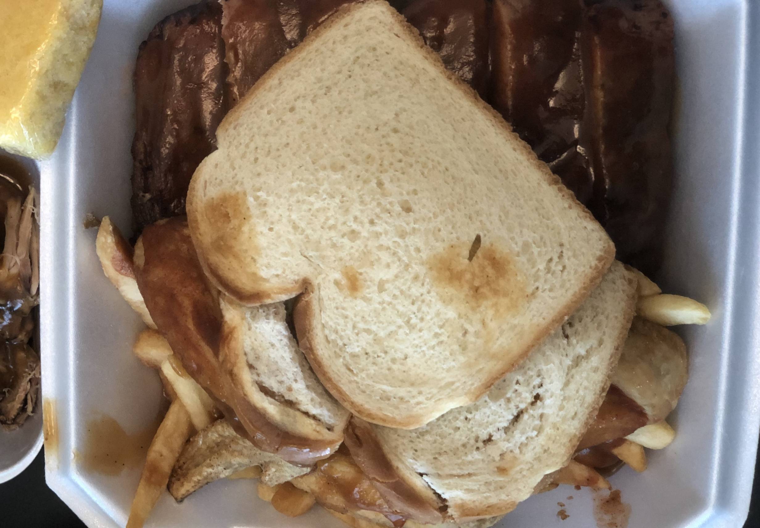 Two slices of white bread lay on top of wings and fries and ribs in a white styrofoam container. Photo by Alyssa Buckley.