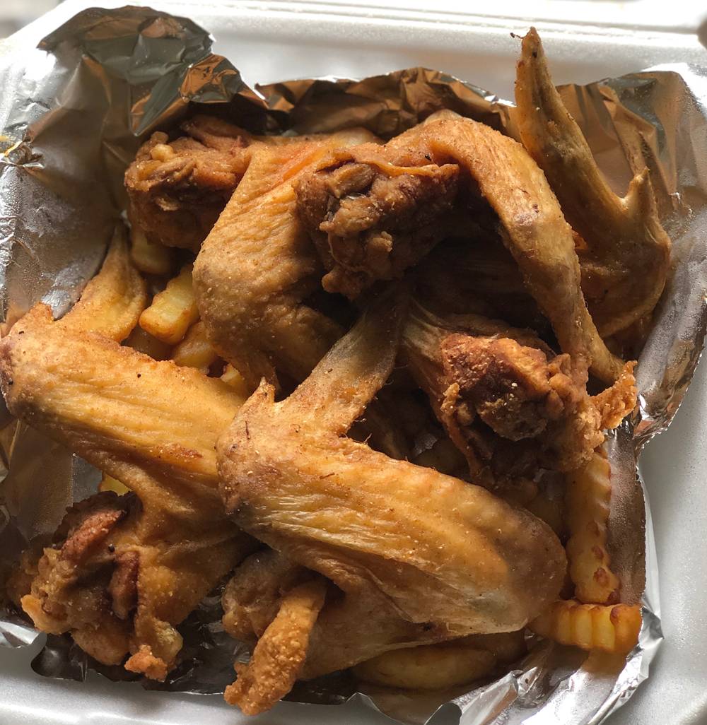 Whole fried chicken wings served on top of crinkle cut fries. The meal is served in a tin foil lined Styrofoam take out container. Photo by Jessica Hammie. 