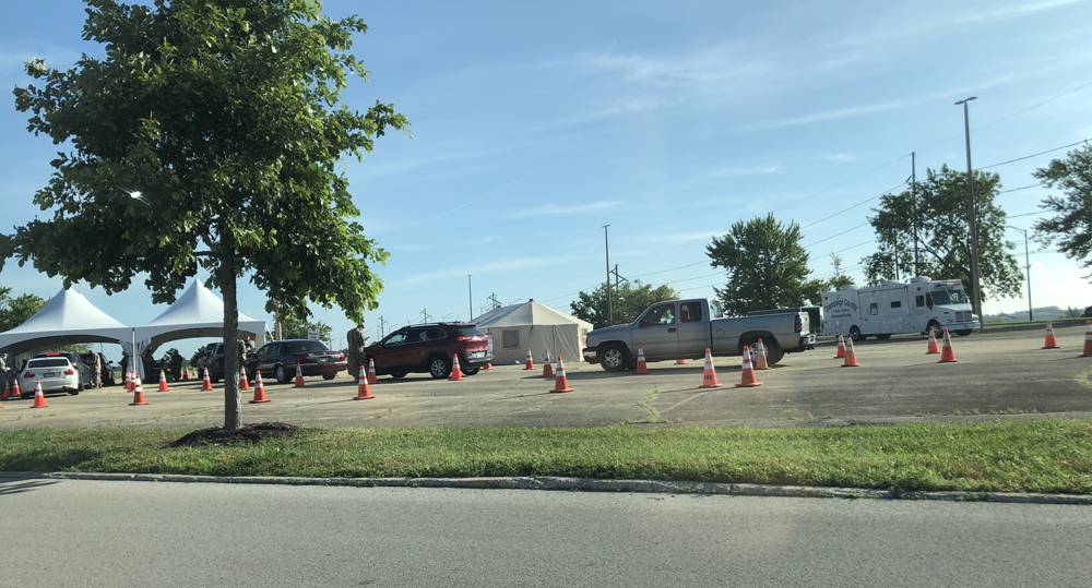 A line of cars at the Marketplace Mall COVID-19 testing site in Champaign. Two lines of cars move toward two white tents. Photo by Jessica Hammie. 