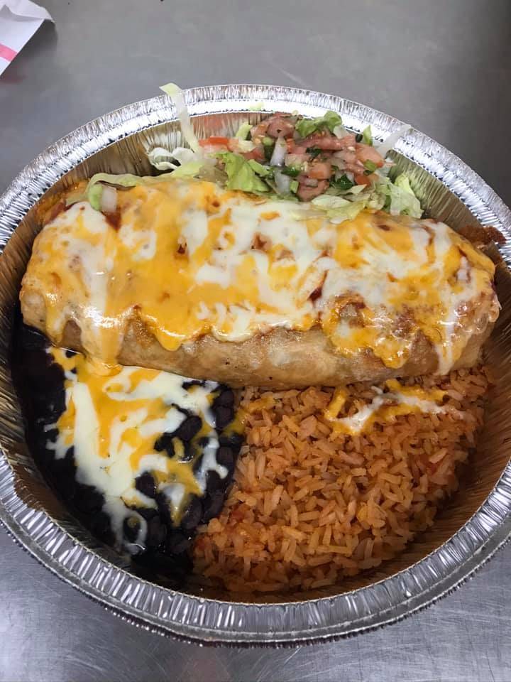 A chimichanga is covered in cheese in a round aluminum carryout container with rice and beans. Photo from Fiesta Cafe's Facebook page.