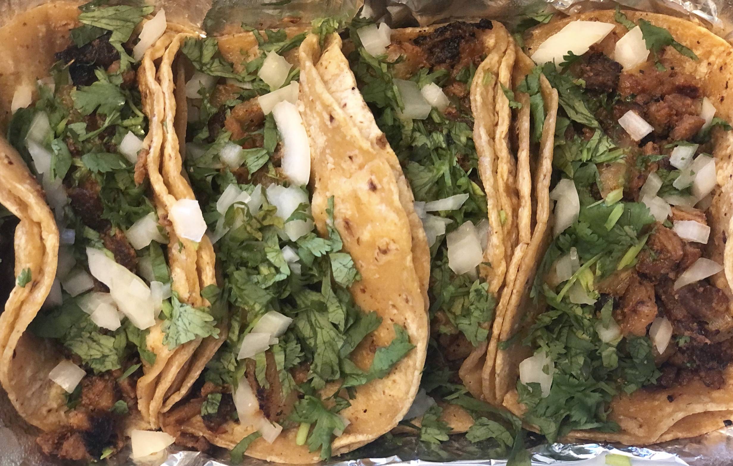 Four al pastor tacos on corn tortillas served Mexican style with lots of cilantro and raw white onion on each. Photo by Alyssa Buckley.