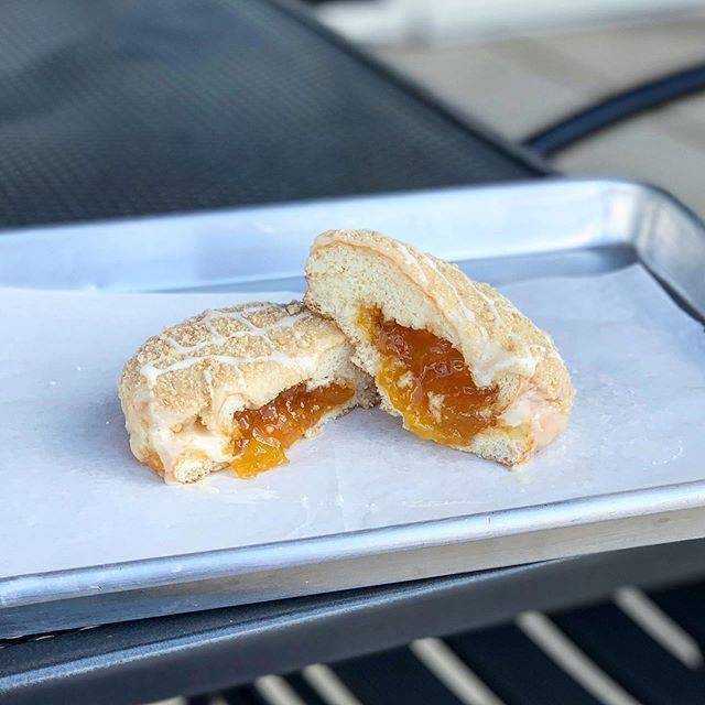 A pastry with a yellow filling it cut in half on parchment paper on a metal tray. Image from Pandamonium Doughnuts Instagram.