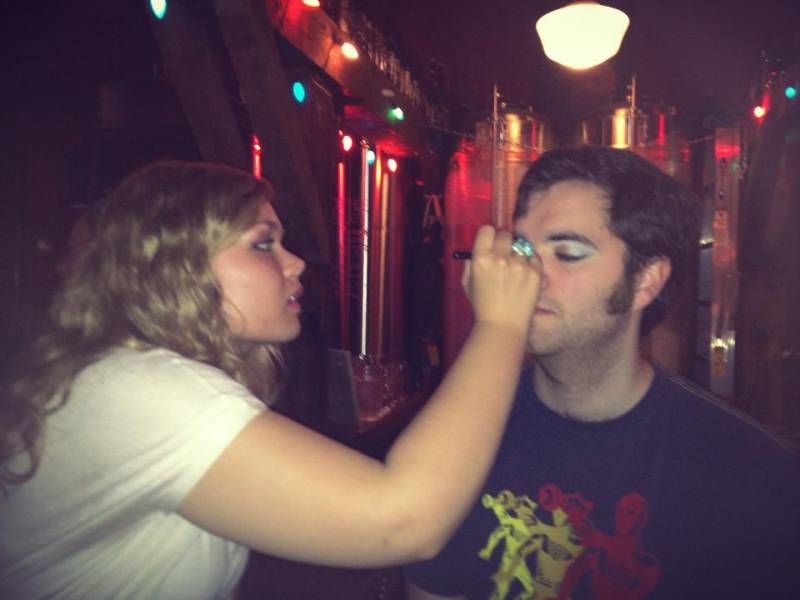 A blond woman is putting eyeshadow on the writer as he sits with his eyes closed. Photo by Lauren Graham.