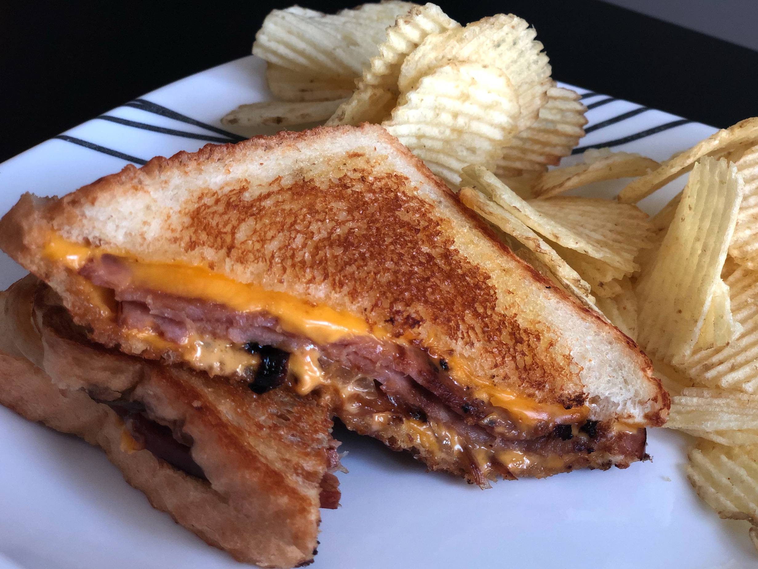 A sliced ham and grilled cheese sandwich from Merry Ann's Diner is on a white plate next to a large portion of ridged chips. Photo by Alyssa Buckley.
