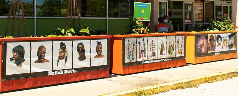 Photo of Common Ground Food Coop raised garden beds from which hang portraits of Black faces by Black artists