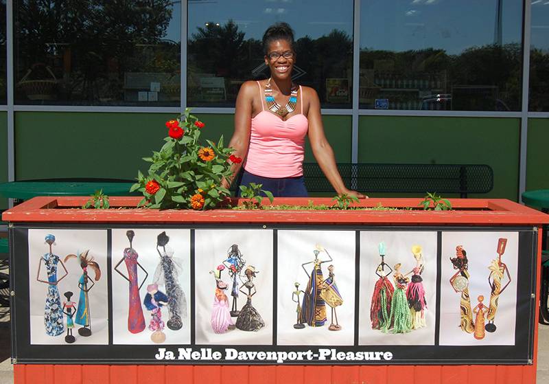 Artist Ja Nelle Davenport-Pleasure with her multipanel installation featuring photos of her handmaid African-inspired sculptures at the Common Ground Food Co-op