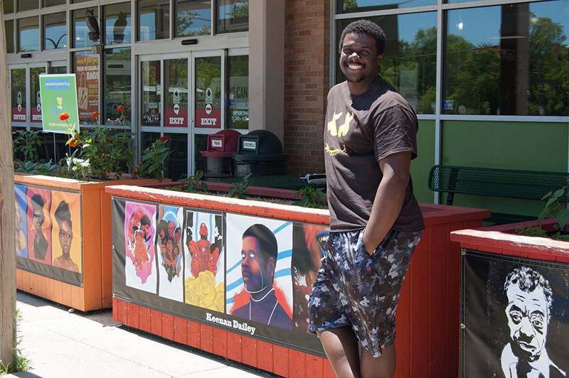 Artist Keenan Dailey standing in front of his multipanel portrait installation outside Common Ground Food Co-op