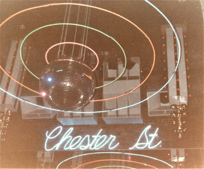 An old photo of a disco ball with a neon Chester St. sign behind it
