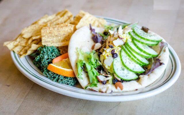 An egg salad pita sits on a plate with a garnish of kale with an orange slice next to a portion of Sunchips. Photo from Cafe Kopi's Facebook page.