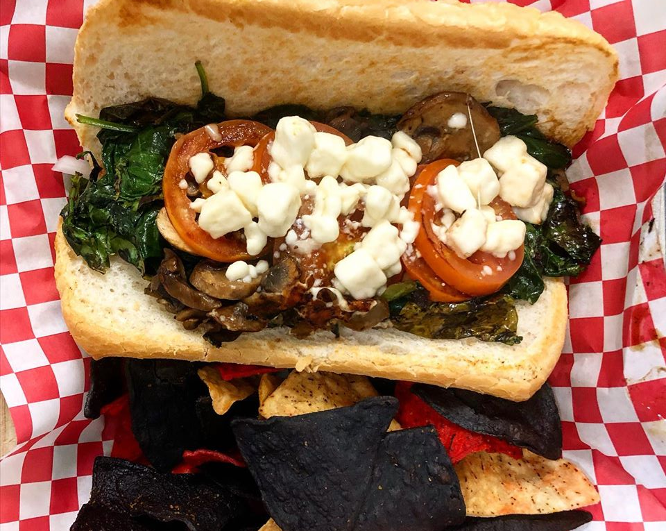 An overhead shot of Farren's Pub's mushroom and spinach sandwich on a baguette. The sandwich is on a red and white checkered paper with tricolor tortilla chips. Photo from Farren's Pub Facebook page. 