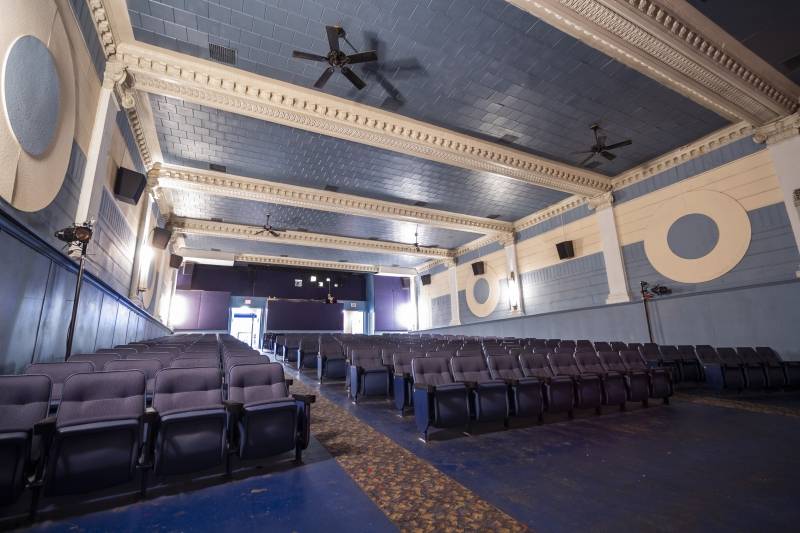 The interior of a movie theater facing the seats. The walls and ceiling are blue with off-white detailing. The blue theater seats are separated into three sections, with carpeted aisles running between them. Photo by Matt Wiley.