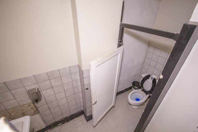 An overhead shot of a bathroom stall. The floor has small white hexagonal tiles and the walls have white square tiles. Photo by Matt Wiley.