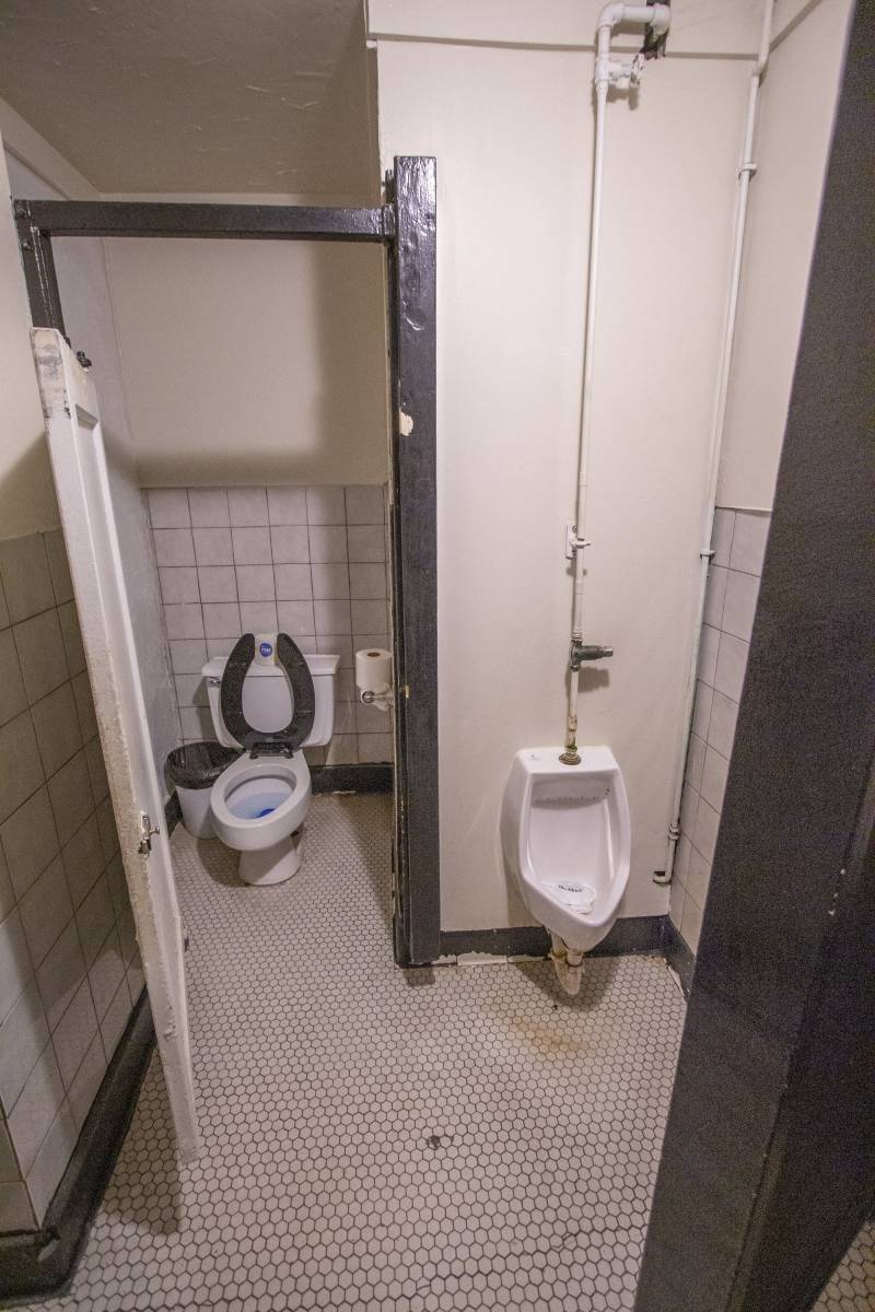 A bathroom stall with a toilet and a urinal side by side. Photo by Matt Wiley.
