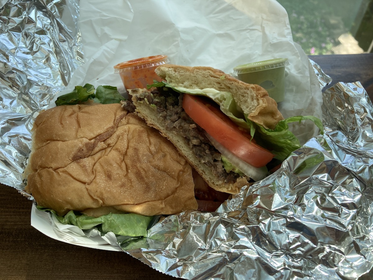 A steak torta with lettuce, tomato, and sour cream with a small plastic side cup of red salsa is in a tin foil lined takeout container. Photo by Anthony Erlinger.