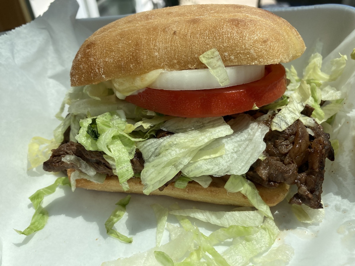 A steak torta on a ciabatta-like bun from Fiesta Cafe sits on white parchment paper in a to go container. Photo by Anthony Erlinger.