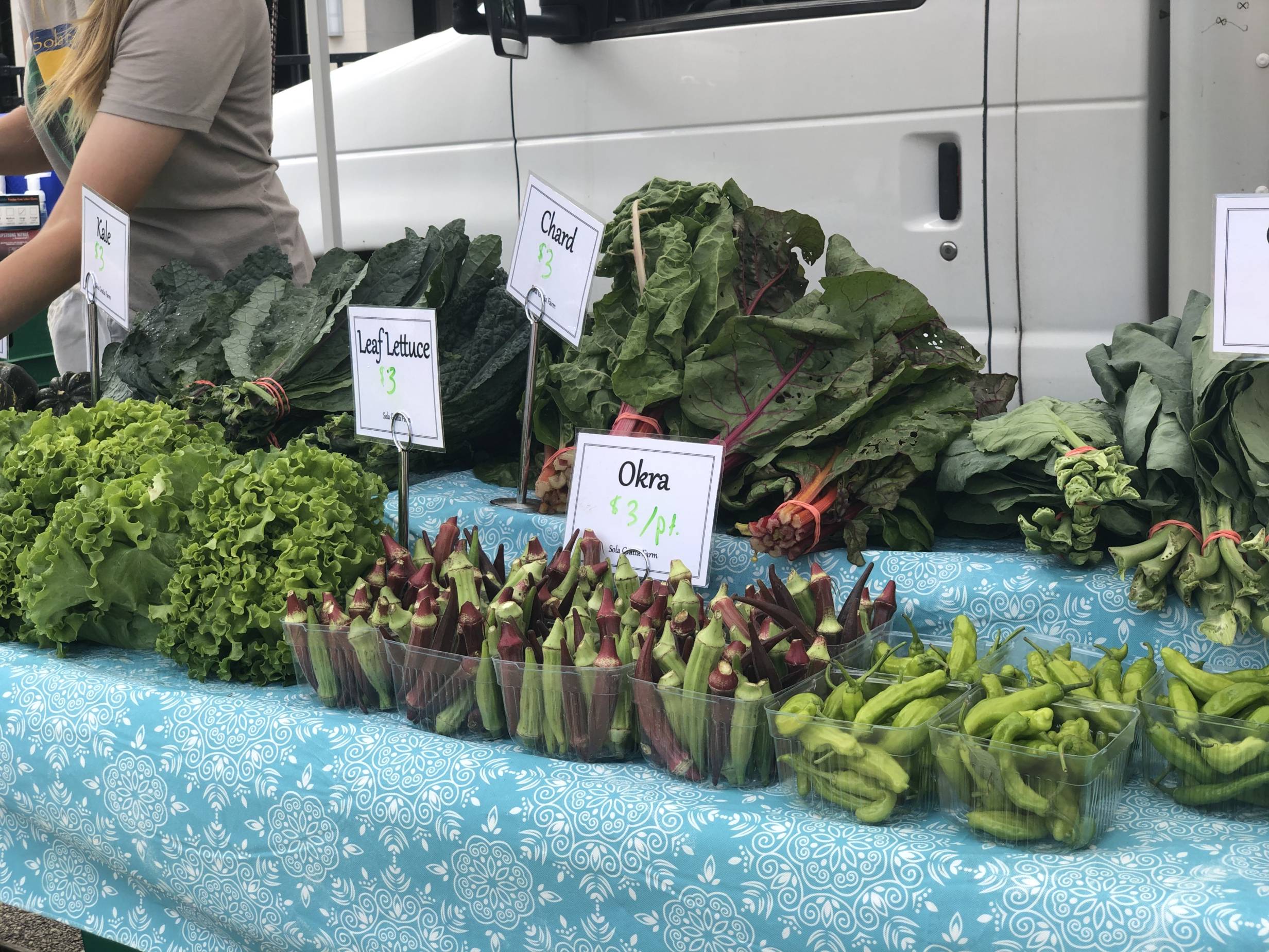 Greens and okra are for sale on a blue tableclothed table at the Champaign Farmers Market. Photo by Alyssa Buckley.
