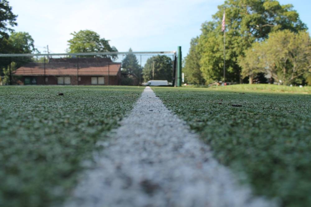 A picture of a synthetic grass turf tennis court, taken from the ground on the baseline and right sideline