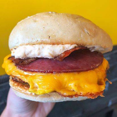 A breakfast sandwich with egg, cheese, bacon, Canadian bacon, and hashbrowns is in clear focus with a yellow background. Photo provided by Cracked.