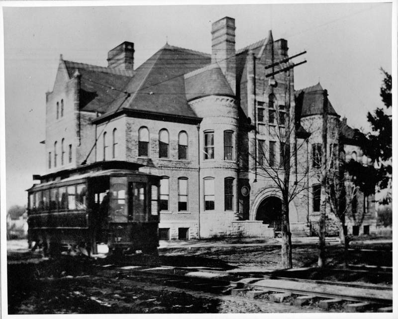Black and white photo of Thornburn School with trolly passing along Springfiled Avenue in front. Two story brick building with multiple gables and round towers. Photo from Digital Collections, University of Illinois.