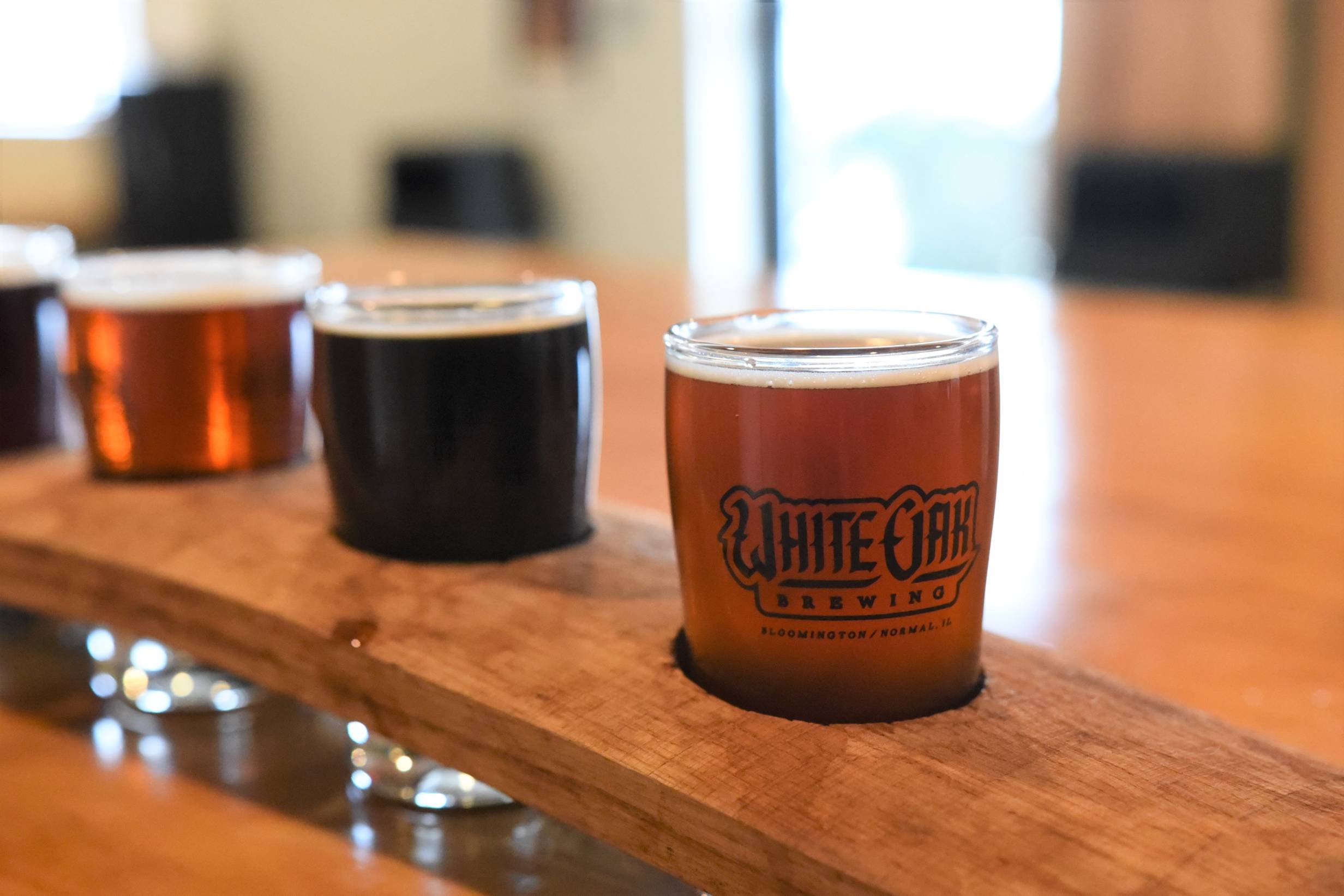 A flight of White Oak beer comprised of their amber ale, dark wheat, and stout. The flight is on a wooden table inside of the brewery. Photo by Jordan Goebig