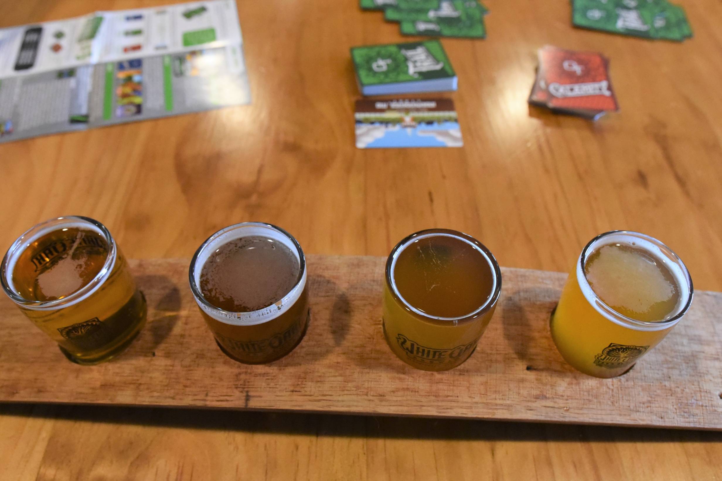 A wider image of the light beer flight from White Oak Brewing. The top of each beer is focused on. The glasses are on a wooden table and a board game is in the background. Photo by Jordan Goebig.
