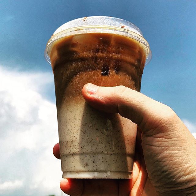 A white hand holds a plastic to-go container of an icy coffee drink from Cafe Kopi with a blue sky in the background. Image from Cafe Kopi's Instagram.
