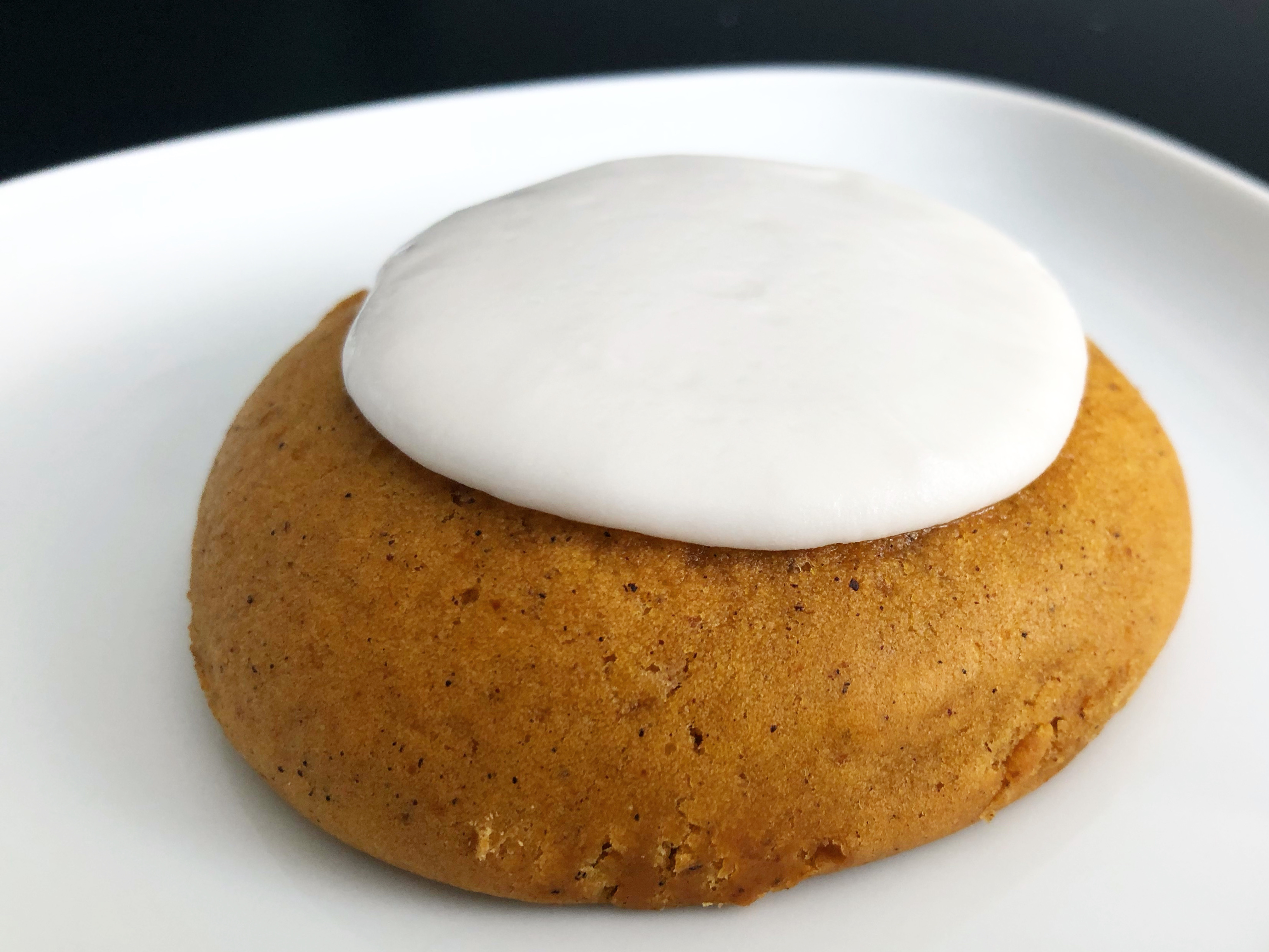 A pumpkin cookie from Art Mart with a yellow-brown cookie base and a white circle of icing sits on a white plate. Photo by Alyssa Buckley.