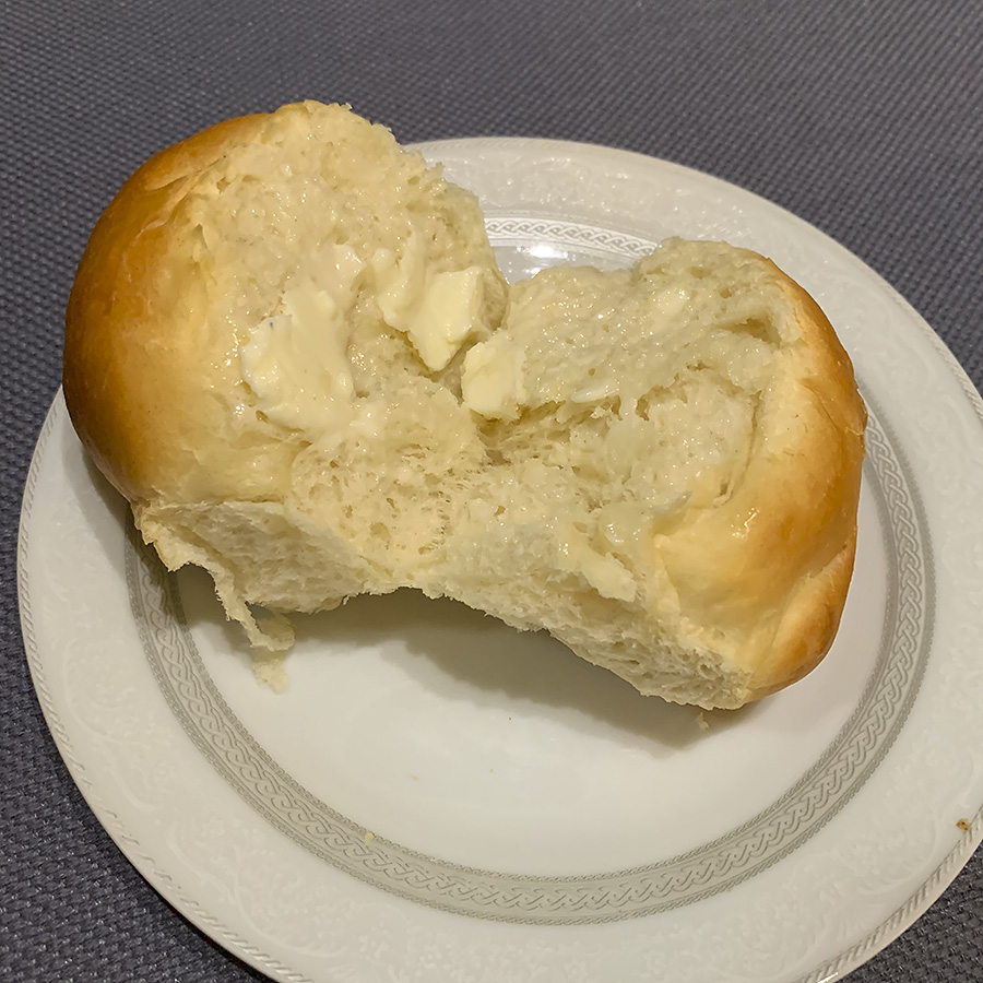 A yeast roll from Old Time Meat & Deli is baked, spit in half, and buttered on a white plate. Photo by Zoe Valentine.