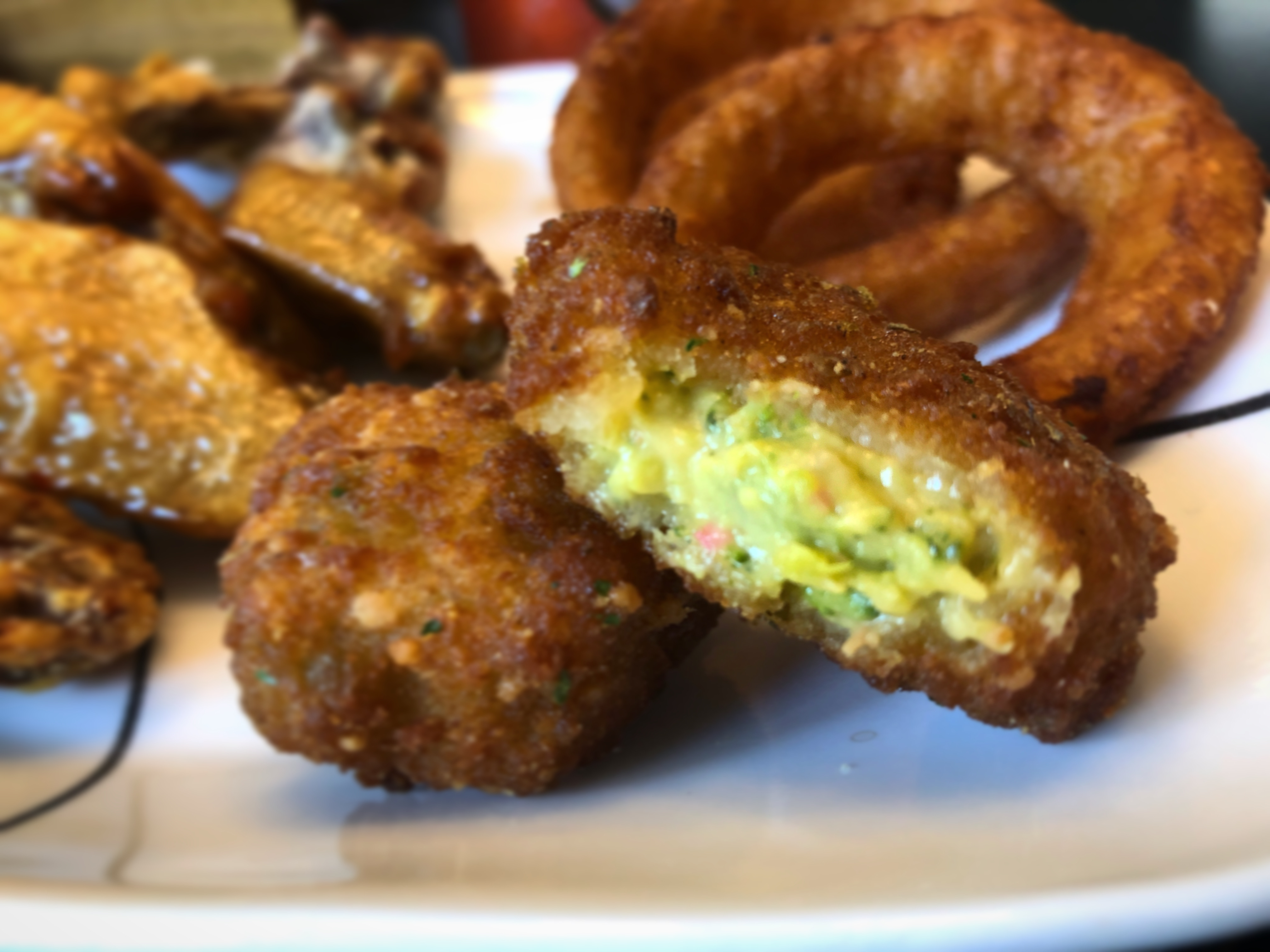 Broccoli bites from Rumbergers are on a plate with wings. The broccoli bite is cut in half to see the cheesy inside. Photo by Alyssa Buckley.
