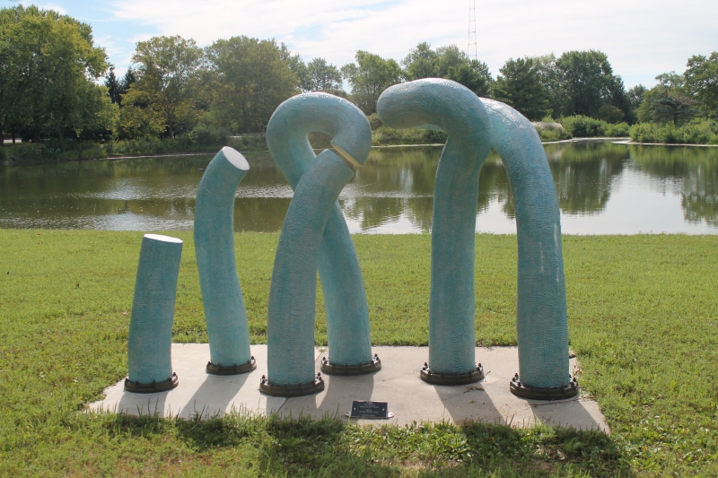 A picture of a light bluw modern quasi-absurdist sculpture, with tentacle like arms coming out of the ground 