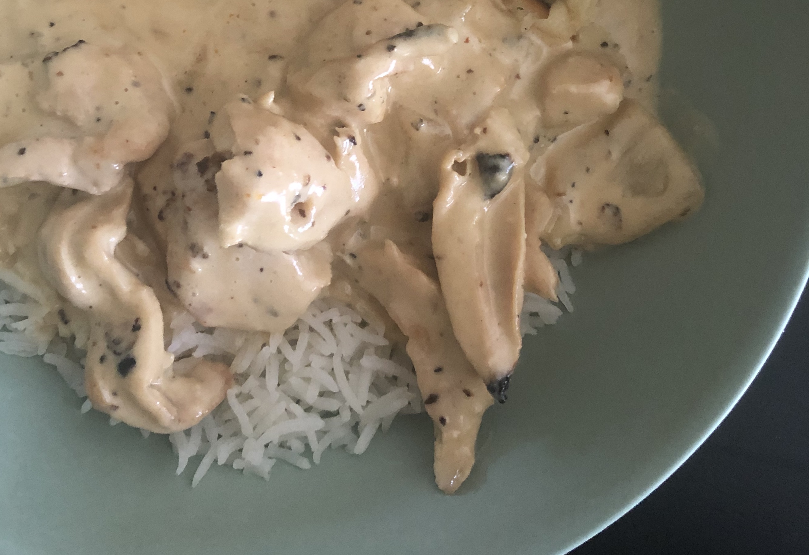 Malai chicken with a white herby sauce is layered over white rice in a light green bowl. Photo by Alyssa Buckley.