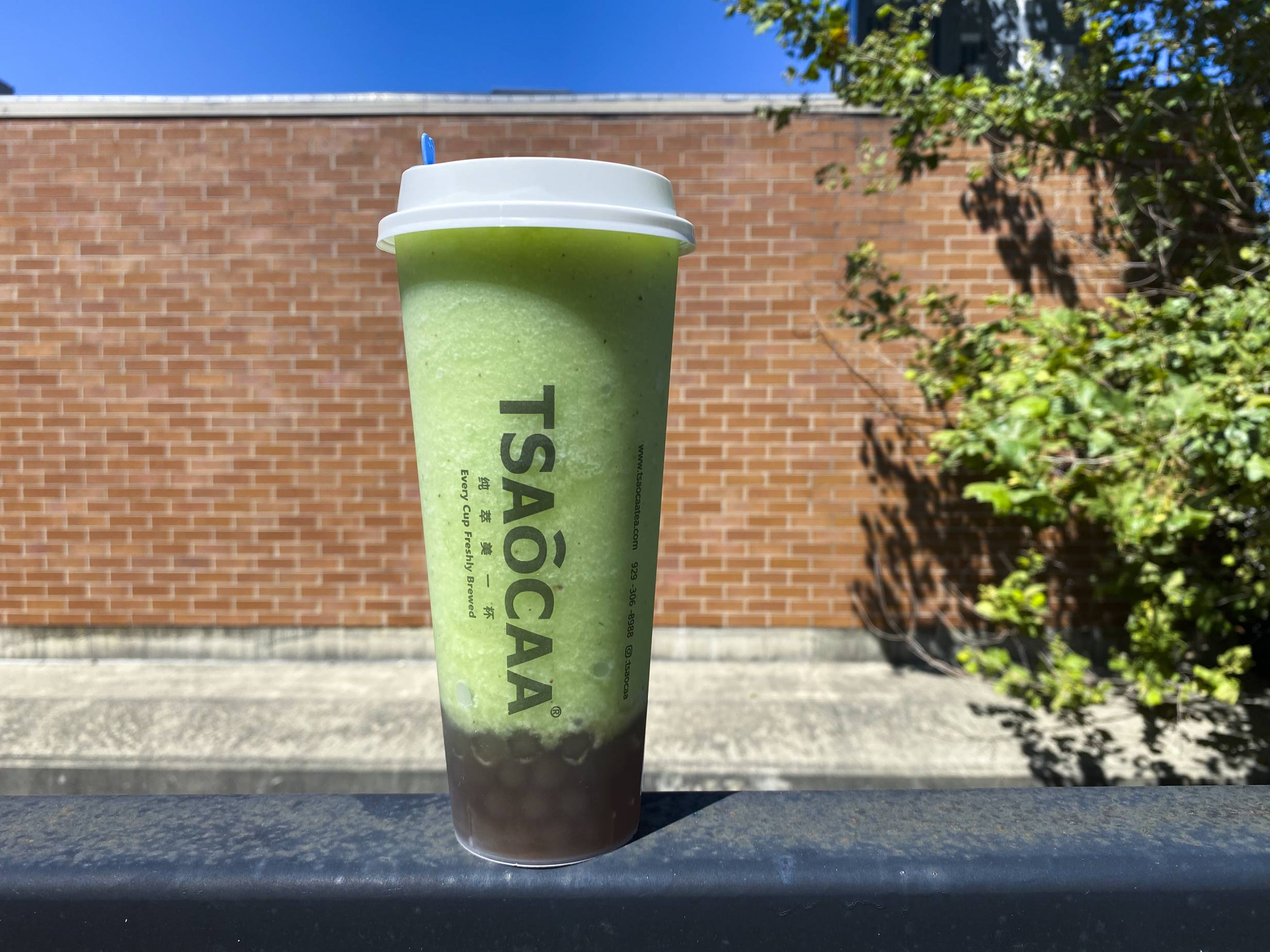 A green kiwi smoothie from Mitsu & Tsaocaa balances on a black railing in an outdoor setting in Champaign, Illinois. Photo by Chantal Vaca.