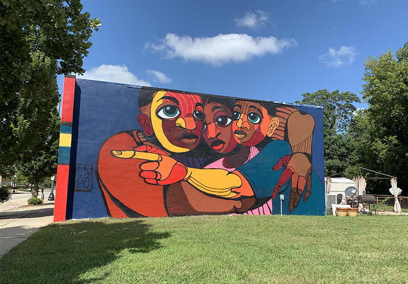 Wide view of Langston Allred's new mural featuring three Black men huddled together in an embrace, located on North First Street in Champaign.. Photo by Debra Domal 
