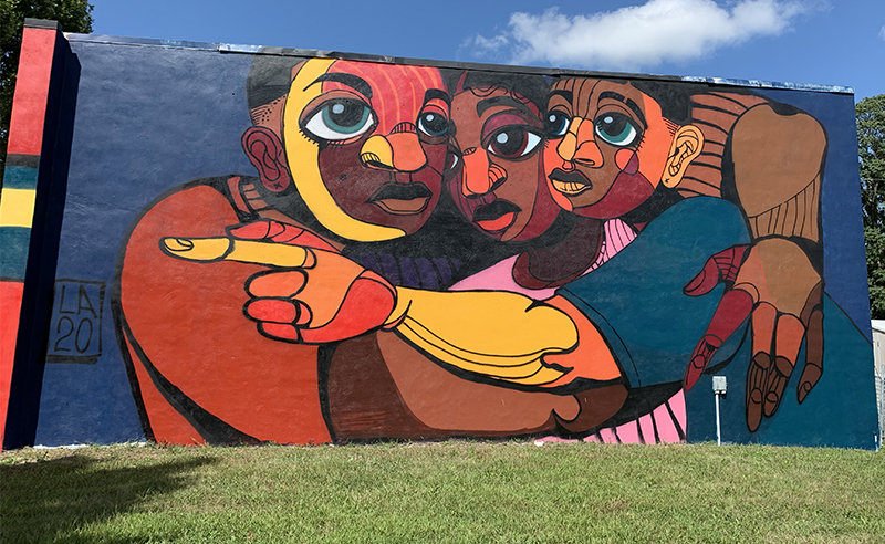 Full view of Langston Allred's new mural featuring three Black men huddled together in an embracel. Photo by Debra Domal  