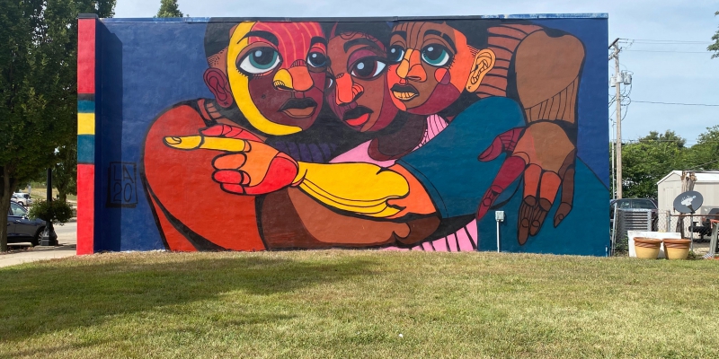 A picture of a colorful mural on First street in Champaign showing three Black youth embracing 