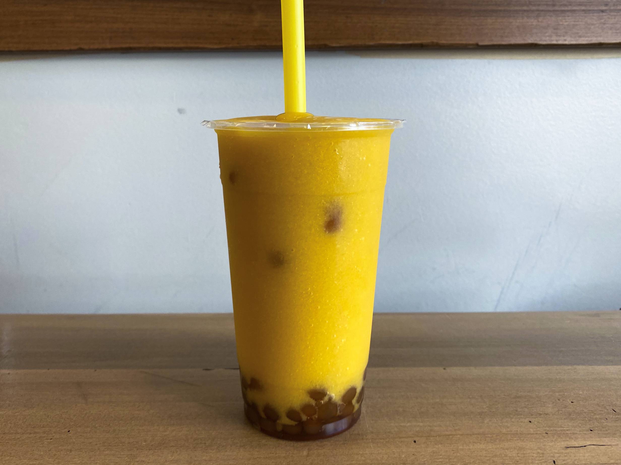 A mango smoothie from Latea with purple boba on the bottom sits on a wooden table. Photo by Chantal Vaca.