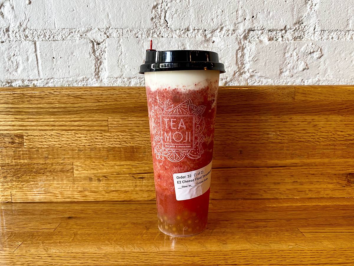 A tall cheese float strawberry smoothie from Teamoji sits on a honey-colored wooden counter with a wooden backplash against a painted-white concrete wall. Photo by Chantal Vaca.