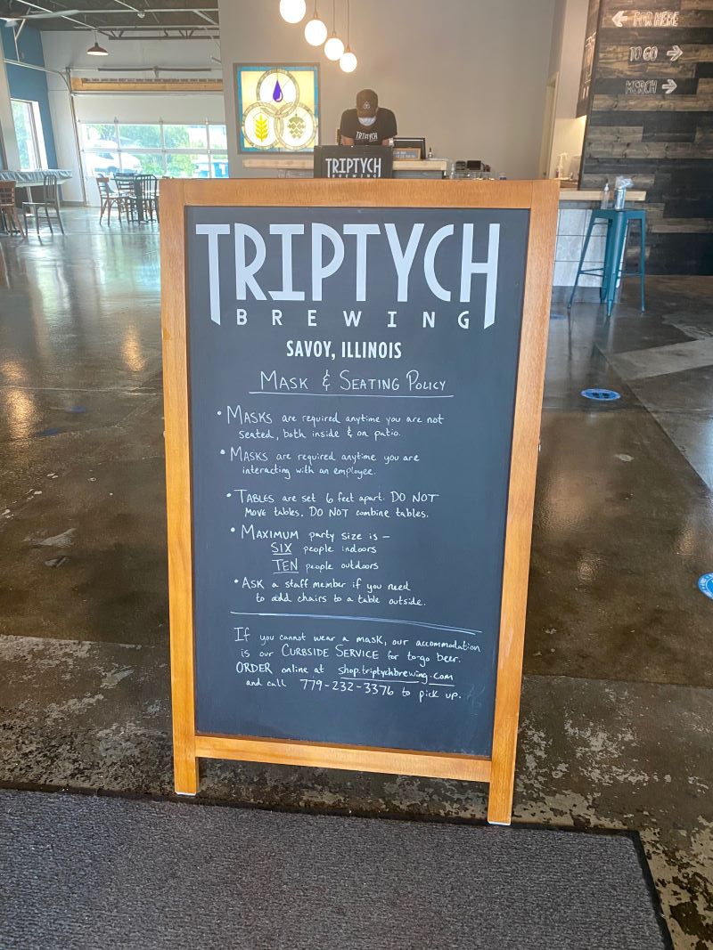 A chalkboard sign that says Triptych Brewing at the top. It has a list of mask and seating guidelines. Photo by Julie McClure.