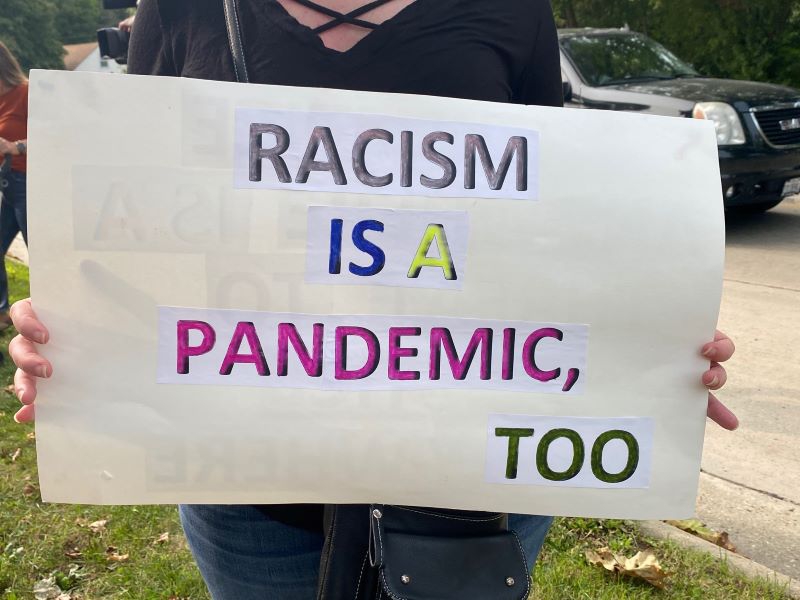A white sign with different colored lettering that says Racism is also a pandemic. Photo by Julie McClure.