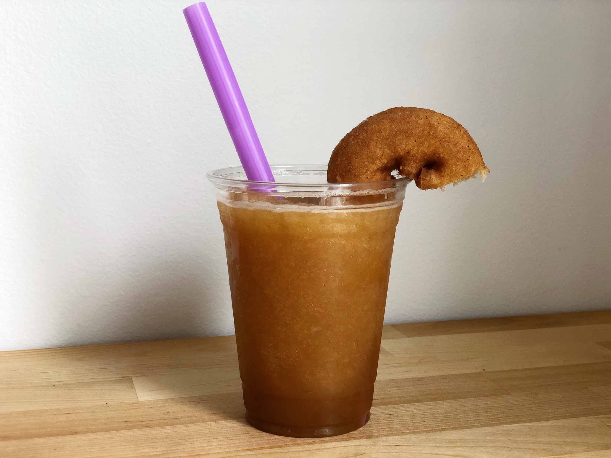 An apple cider slush from Watson's Shack & Rail with a purple straw and a half-donut garnish sit on a butcher block counter. Photo by Alyssa Buckley.
