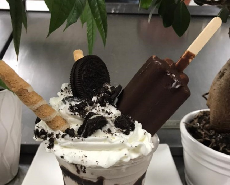 A deluxe Oreo milkshake with an Oreo, chocolate pirouette, and a chocolate ice cream treat sticking out of a tall, plastic cup filled with Oreo ice cream. Photo by El Oasis.