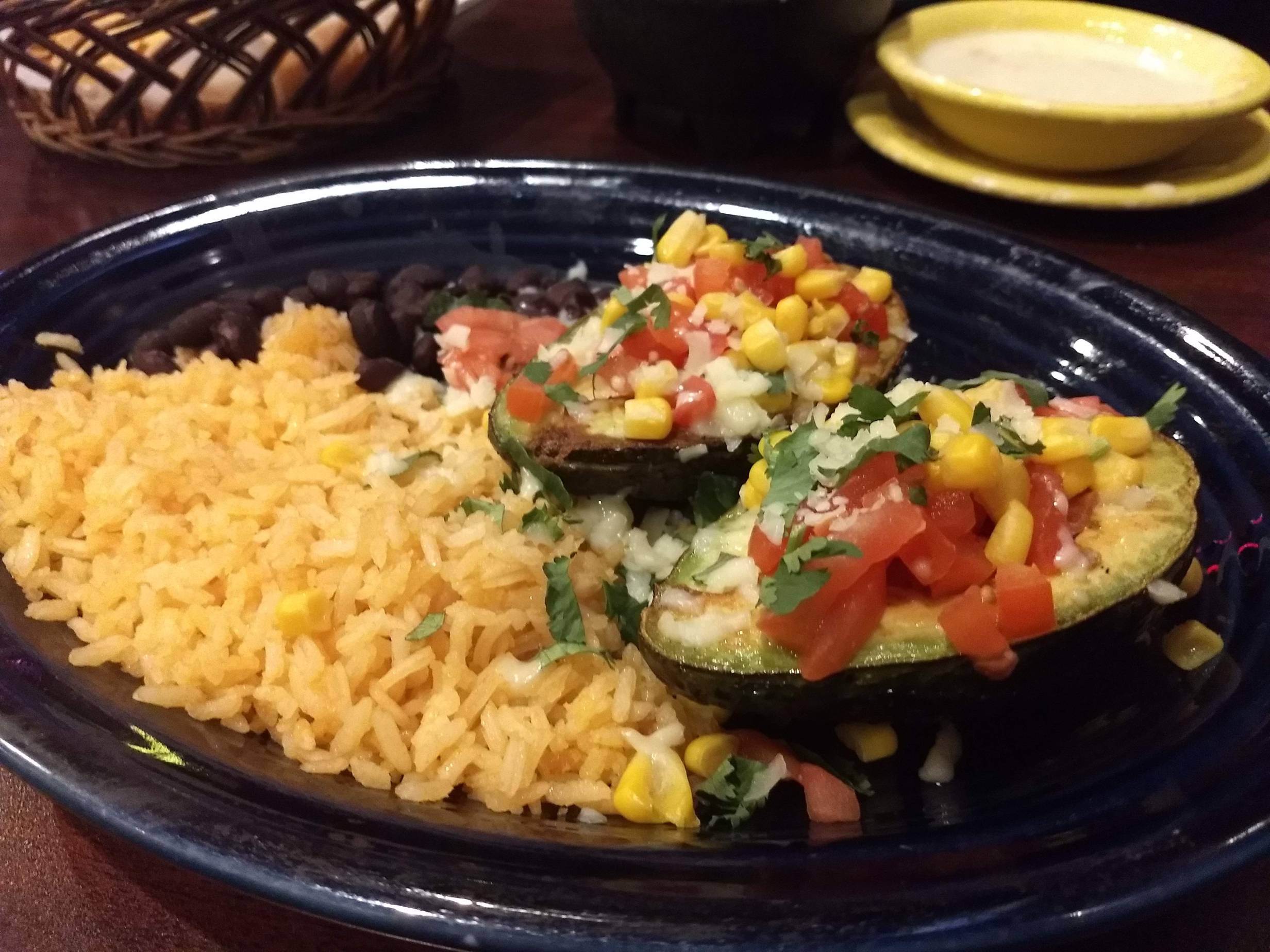 Stuffed Avocadoes from El Toro. One whole avocado cut in half and filled in the middle with black beans, topped with cheese and a fresh corn and tomatoe salsa. To the left is a side of riceand black beans. Served on a blue plate. Photo by Adam Rahn. 