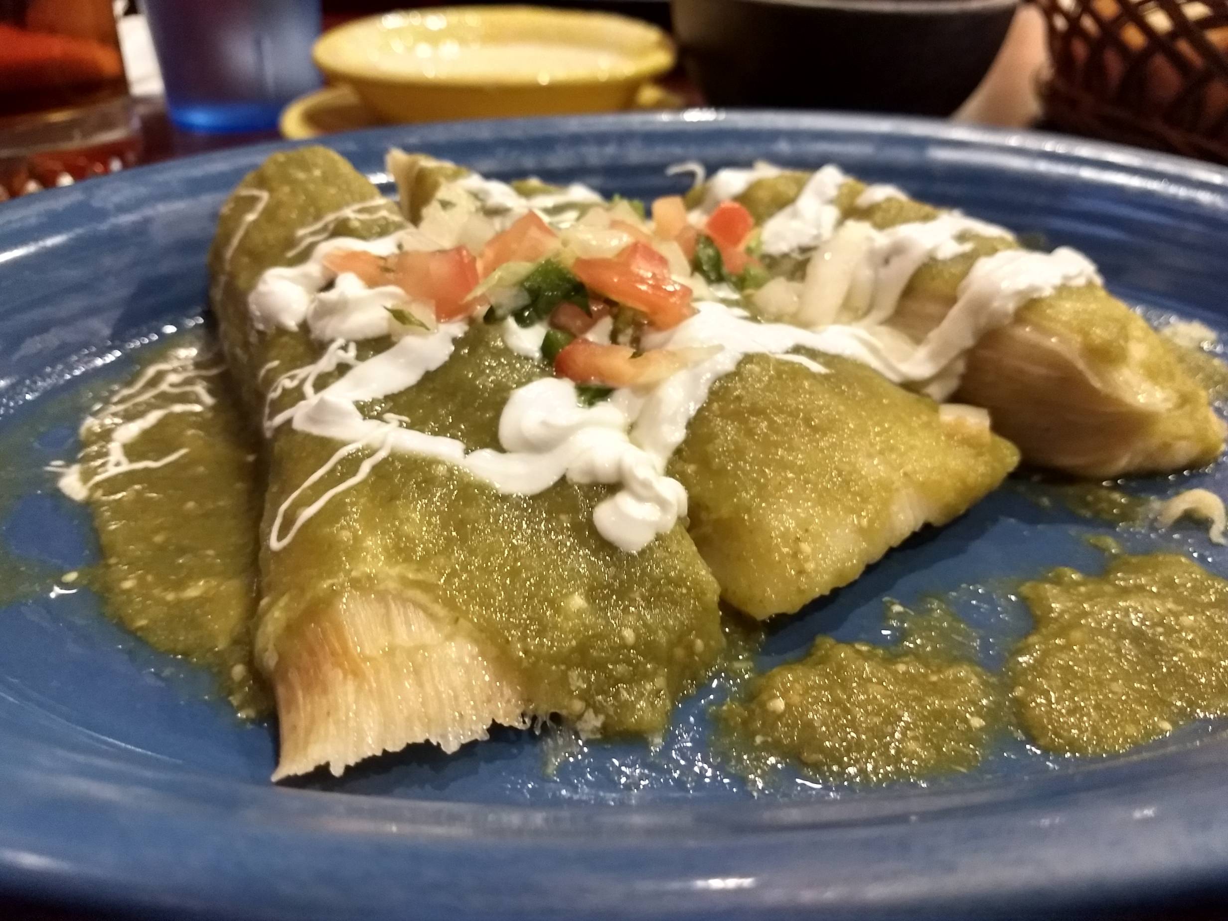 Vegetarian tamales from El Toro. Close up of three tamales covered in green salsa, sour cream, and pico de gallo. Served on a blue plate. Photo by Adam Rahn. 
