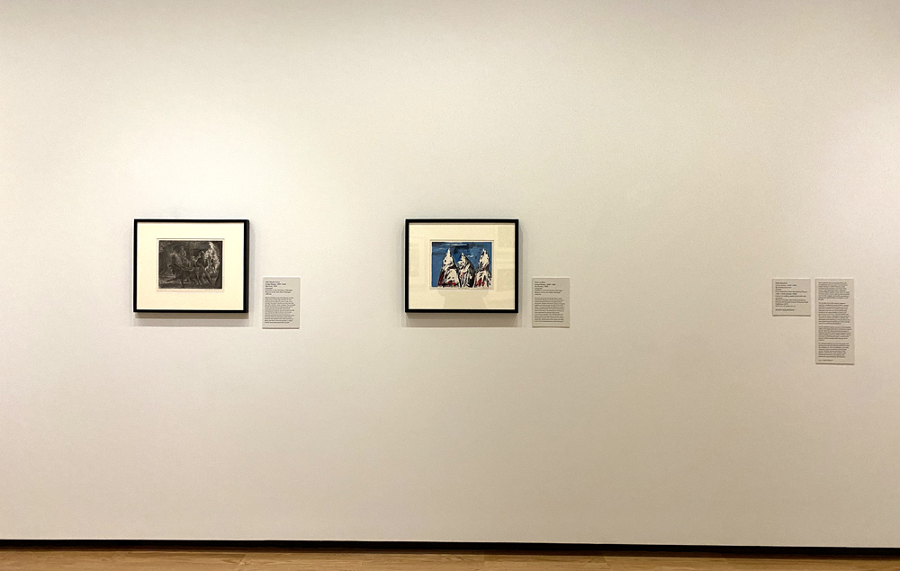 Installation view from exhibition Pressing Issues at Krannert Art Museum. Two horizontally oriented framed works with black frames are hung on a wall. To the right is a blank space where artwork should be. To the right of the blank space are two wall labels. Photo by Jessica Hammie. 