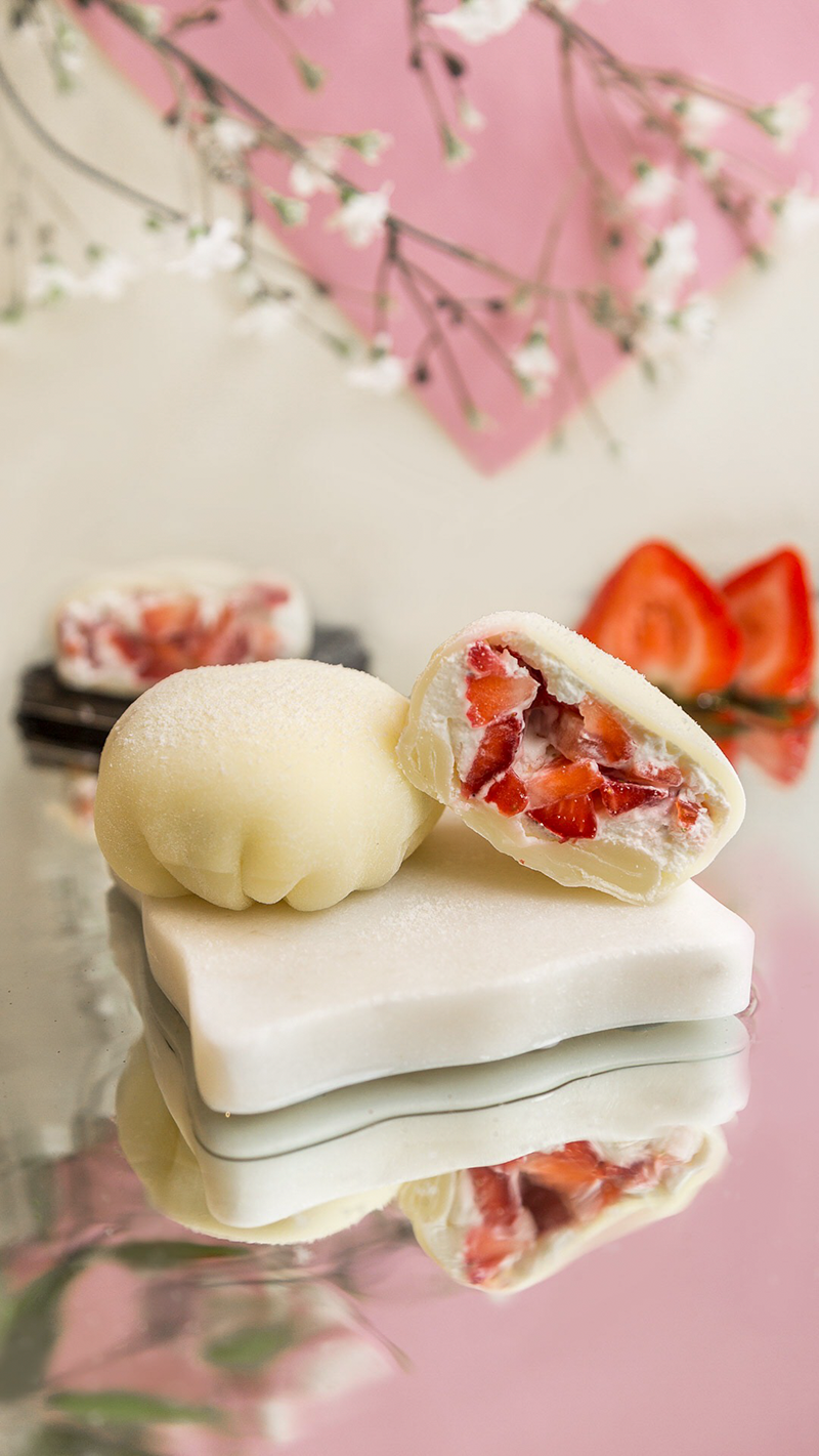 Two sticky rice balls, one sliced open revealing the chopped strawberries inside the pastry, sit on a white plate. Photo by Teamoji.