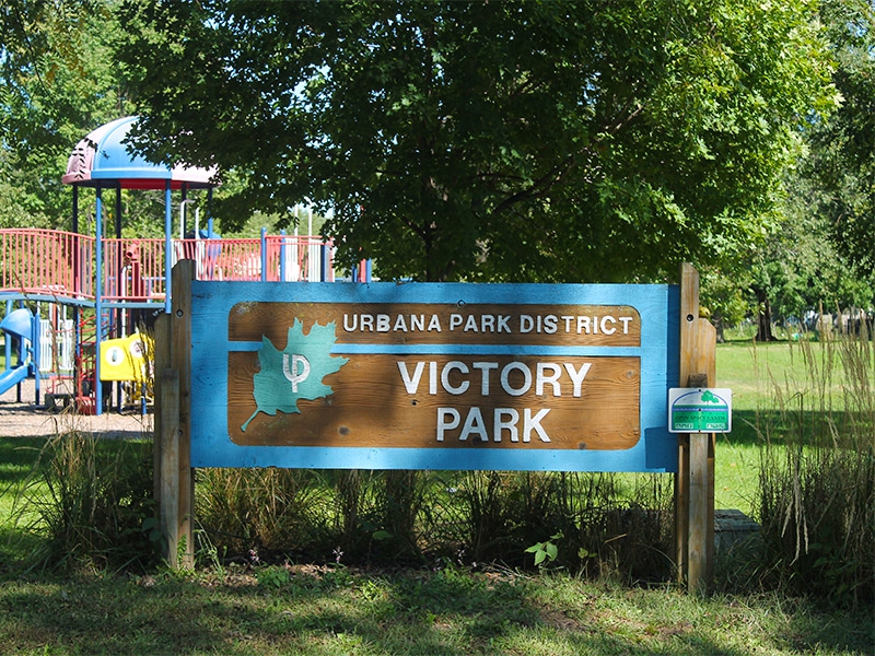 A sign that states Victory Park with a playground in the backdrop 