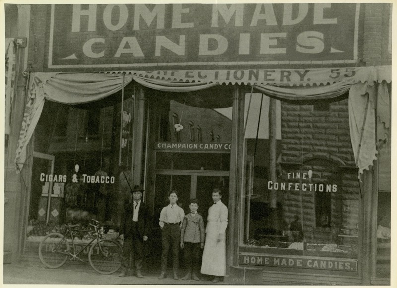 â€œChampaign Candy Companyâ€ First Vrinerâ€™s store at 55 Main Street, Champaign, about 1904, before Vriner completely remodeled the front and interior of the store around 1907-08. Man wearing hat is Peter Vriner. His partner George Vaky is to the right in the white apron. (Champaign County Historical Archives, The Urbana Free Public Library, Urbana, Illinois).