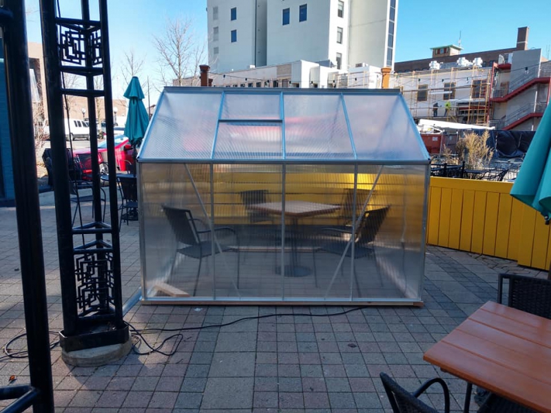 A small greenhouse sits on a patio. There is a table and chairs inside. Photo from Aroma Cafe Facebook page. 