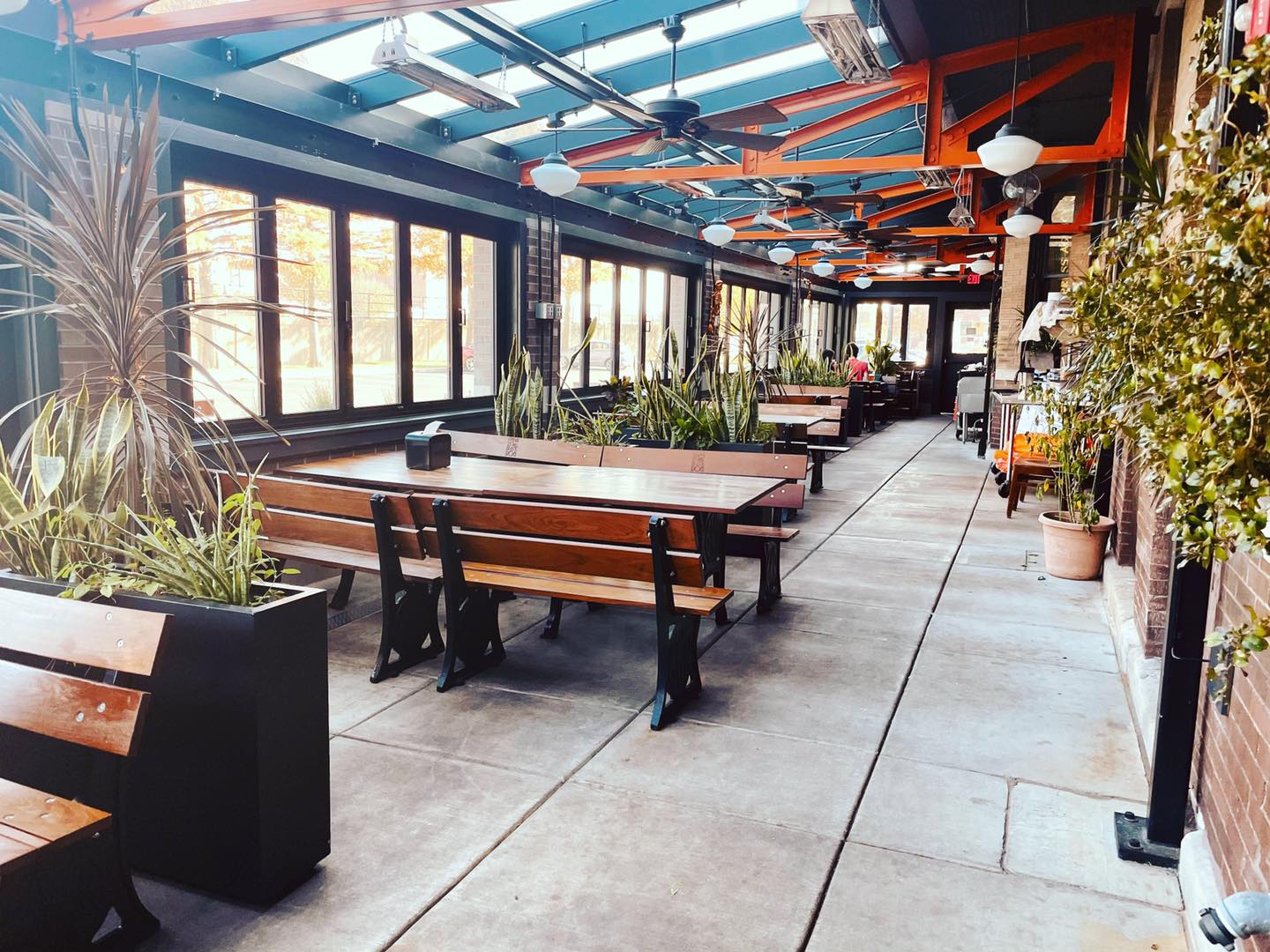 Inside of Black Dog Champaign's four season porch during the daytime, there are several tables with bench seating on a concrete flooring with overhead radiant heating. Photo by Alyssa Buckley.